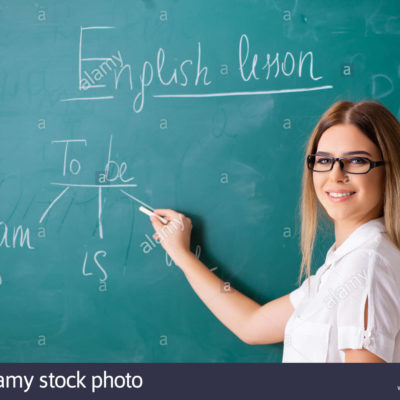 young female english language teacher standing in front of the blackboard RBM9DP